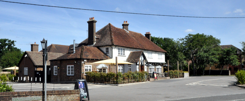 A two-storey brick building with several extensions, and a car park in front