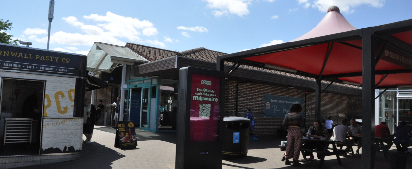 A kiosk, a brick building, and a red canopy over tables and chairs, with people